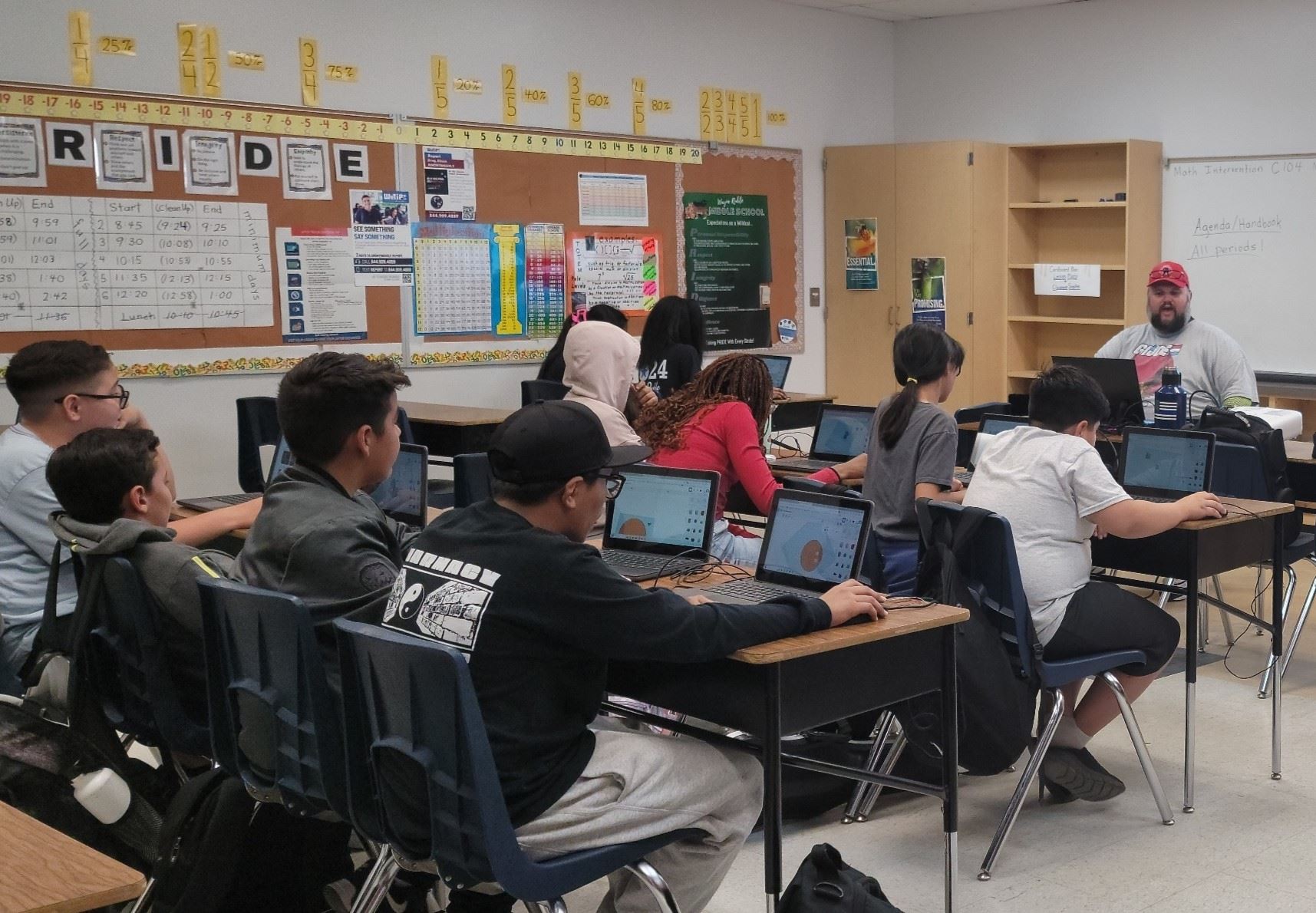 students seated in classroom following instructions on laptops from teacher